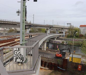 Links zwei Eisenbahnbrücken über Fluss und Straße, rechts ein Bagger und ein Bauwagen auf der Straße