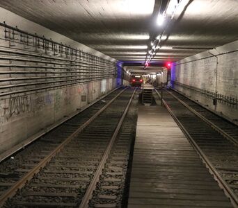 Zwei Gleise in einem Tunnelbauwerk, auf dem linken Gleis fährt ein Zug